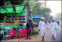 Another waits for customers at right. Note the two young Moplah boys going by dressed in their traditional attire.